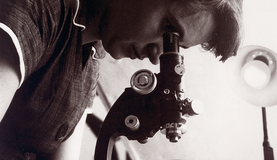 black and white photograph of a scientist looking through a microscope
