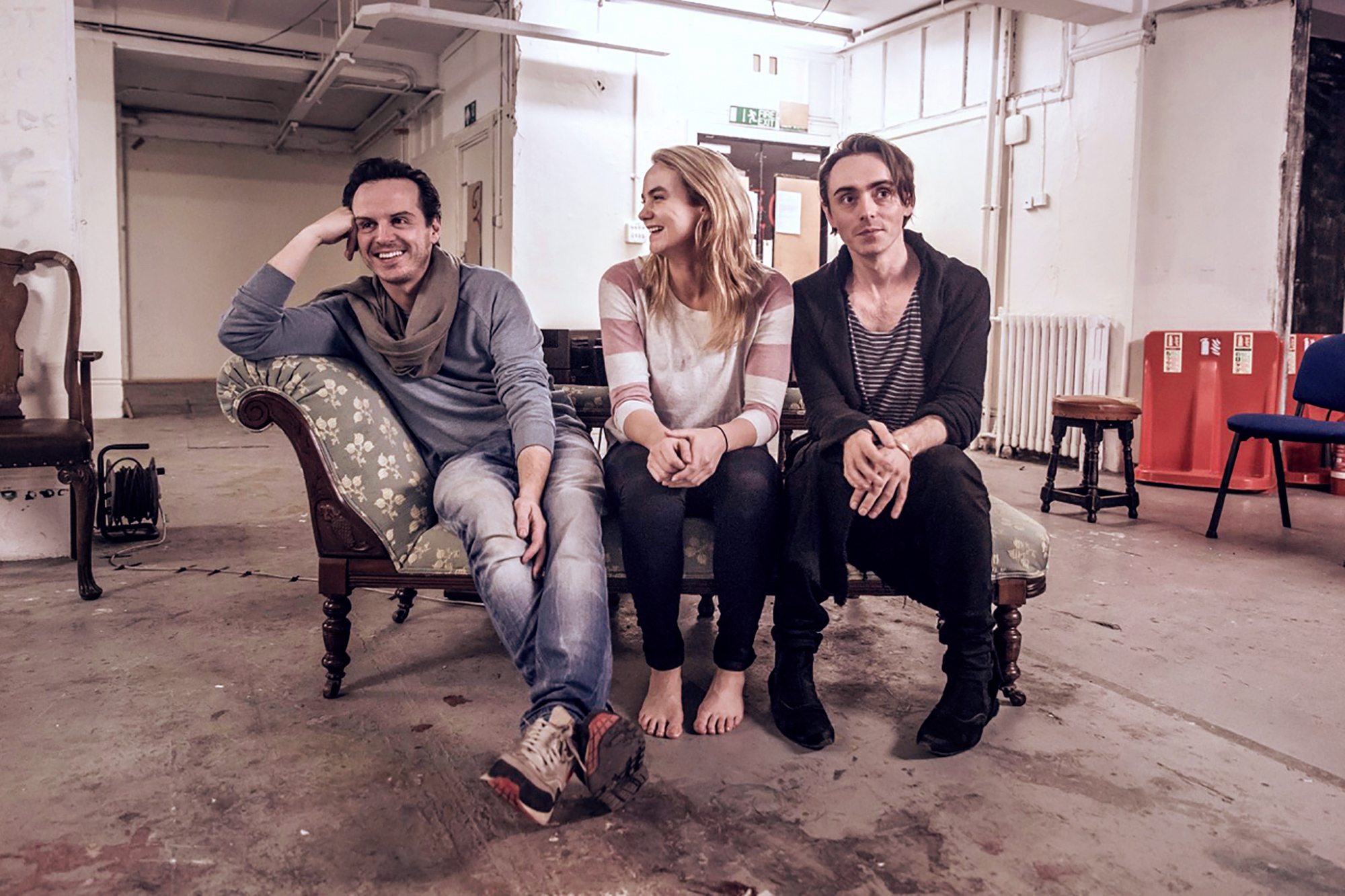 three actors sitting on a sofa, smiling