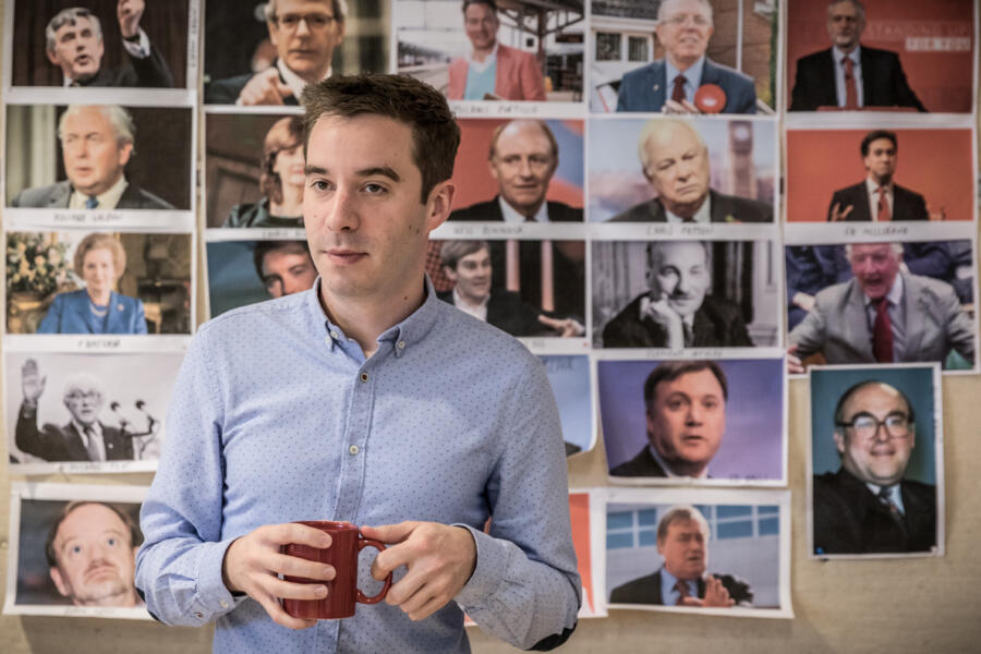 author standing in front of wall covered with politician headshots